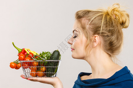 有吸引力的妇女拿着购物篮里面有绿色的红蔬菜闭着眼睛闻建议用灰色的健康高纤维饮食有吸引力的妇女拿着蔬菜有嗅觉图片