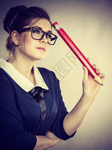 身着书呆子眼镜的学生长得像女戴着书呆子眼镜拿着巨大的铅笔想一些事情图片
