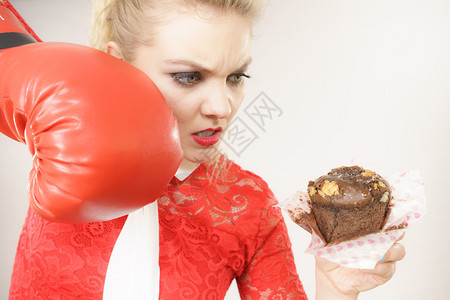 有趣的金发女人拿着美味巧克力蛋糕和拳击手套与坏食物搏斗灰色的女与坏食物搏斗拳击巧克力蛋糕图片