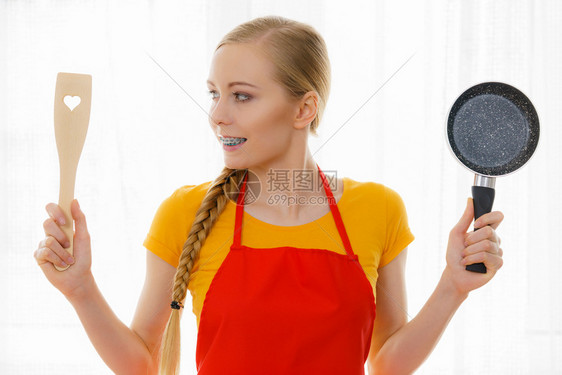 穿着围裙的快乐年轻女子手持小锅和木制烟幕准备在厨房做饭图片