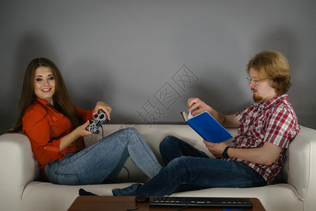 在沙发上坐着一对夫妇在沙发上闲暇时间女人玩电子游戏男人看书女玩游戏男看书图片