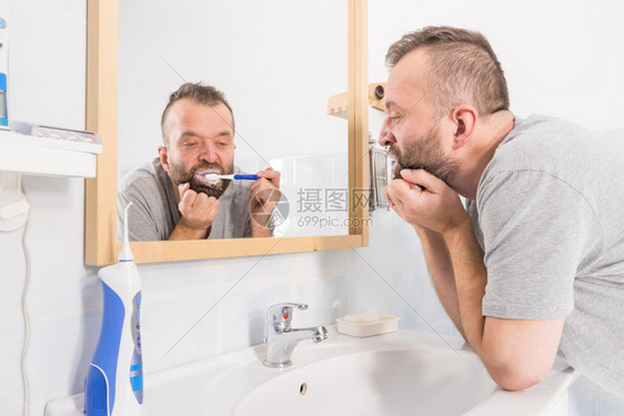 成人男子在清晨卫生例行活动期间在卫生镜上刷牙无聊宿醉或困累图片