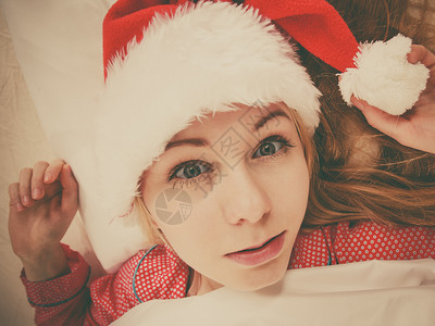 快乐的女士在等待圣诞节穿着睡衣和圣诞老人的帽子躺在床上快乐的女士穿着睡衣和圣诞老人的帽子背景图片