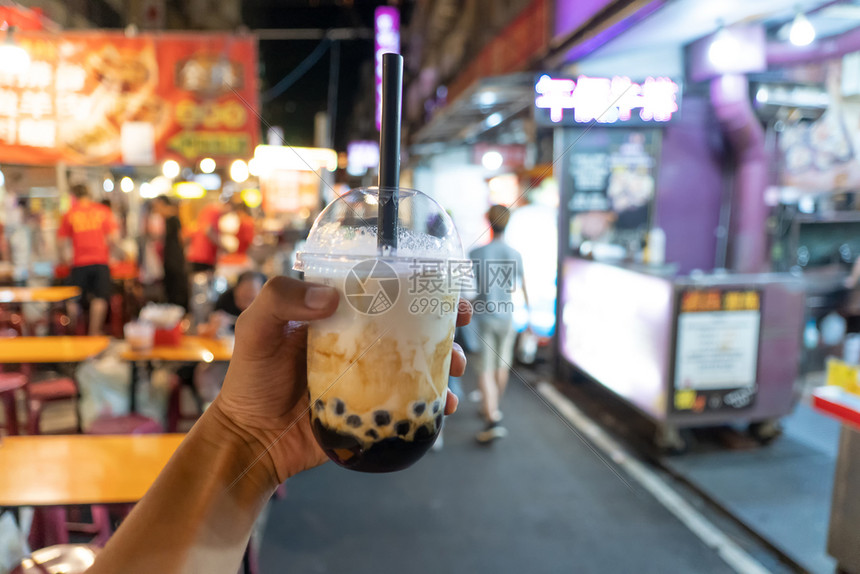 手握着冰奶茶塑料杯底泡沫模糊在夜市的传统饮料图片