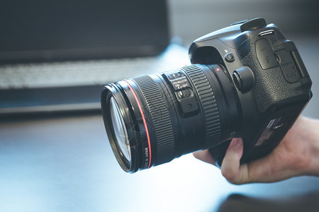 摄影师手上拿着一个专业相机手持远光镜头在模糊背景的笔记本电脑上图片