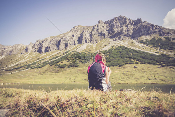 穿运动服的妇女正在徒步时休息坐在地上享受山和湖风景图片