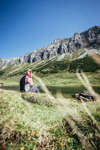 穿运动服的妇女正在徒步时休息坐在地上享受山和湖风景图片