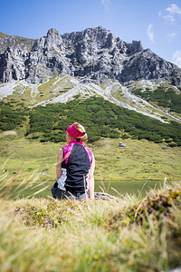 穿运动服的妇女正在徒步时休息坐在地上享受山和湖风景图片