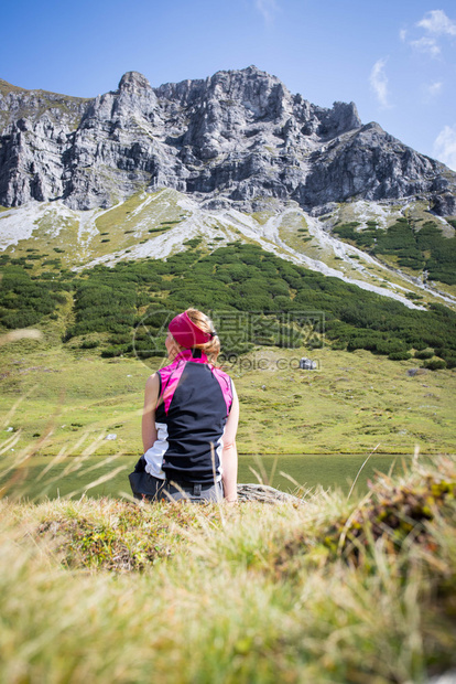 穿运动服的妇女正在徒步时休息坐在地上享受山和湖风景图片