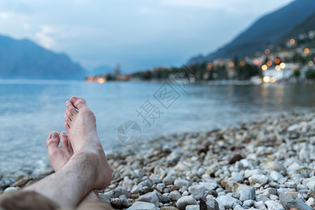 男人坐在石子海滩上享受着夜晚LagodiGarda湖的风景图片