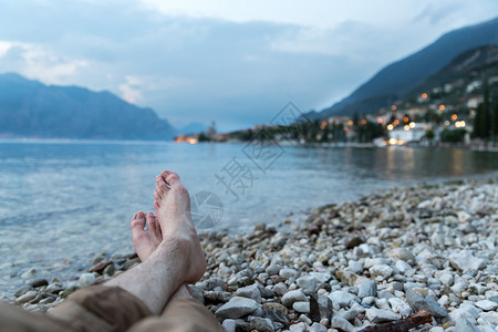 男人坐在石子海滩上享受着夜晚LagodiGarda湖的风景图片