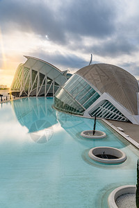 西班牙巴伦亚市科学城的全景电影院游客在城市科学博物馆旁边参观其背景是黎明时有云和太阳图片