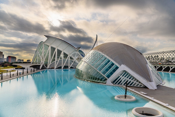 西班牙巴伦亚市科学城的全景电影院游客在城市科学博物馆旁边参观其背景是黎明时有云和太阳图片