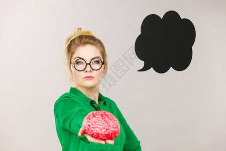 身穿绿色夹克和眼镜的女商人强烈思考寻找大问题解决方案持有假大脑黑色思维或言语泡沫紧地地在着图片