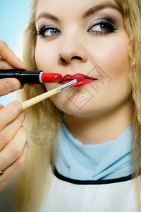 专业化妆艺术家在女时装模特嘴唇上应用红色印或刷子涂口红图片