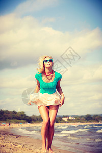 穿着浪漫服装的迷人金发女子在海滩散步和夏天放松图片