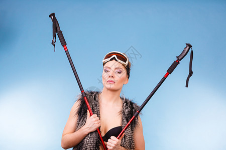 冬季体育活动概念穿着黑色胸罩滑雪护目镜和毛衣手持滑雪杆蓝背景工作室拍摄的微笑女孩身着胸罩和手持滑雪杆的妇女图片