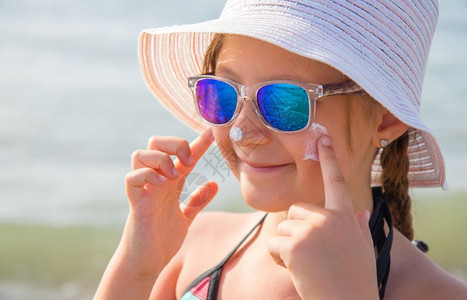 笑着的女孩帽子涂抹保护面霜在海滩上图片
