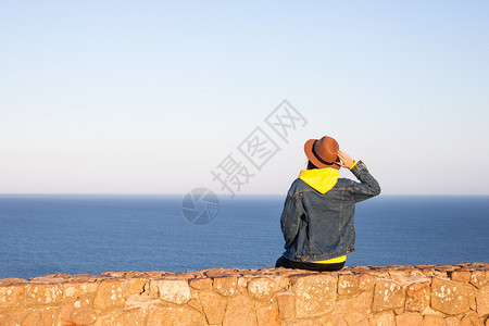 穿旅行服装和戴帽子的妇女坐着看蓝海和天空旅行概念照片坐着和看蓝海天空的妇女图片