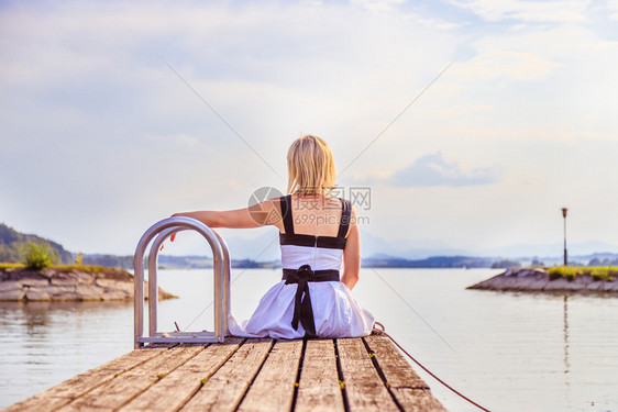 穿白裙子的年轻女孩坐在脚桥上享受湖边的风景图片