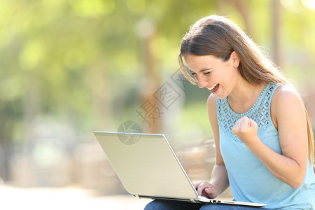 兴奋的女检查笔记本电脑内容在公园庆祝好消息图片