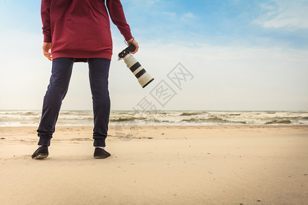 在秋天的气下在海滩上闲暇散步的妇女拥有专业摄影机图片