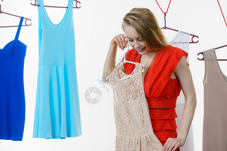 在商店或衣柜里穿服的金发长年轻女子选择夏季服装挂在衣架上的服白出售购物时装和概念在商店里挑衣服在商店里挑衣服图片