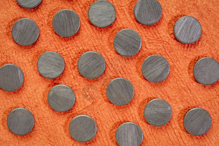 一组小圆形陶瓷发酵磁铁相对于纹理橙皮纸的顶端视图图片