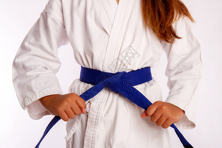 穿着白色传统和服的小女孩在训练或比赛前拉在蓝带上绑空手道带上图片