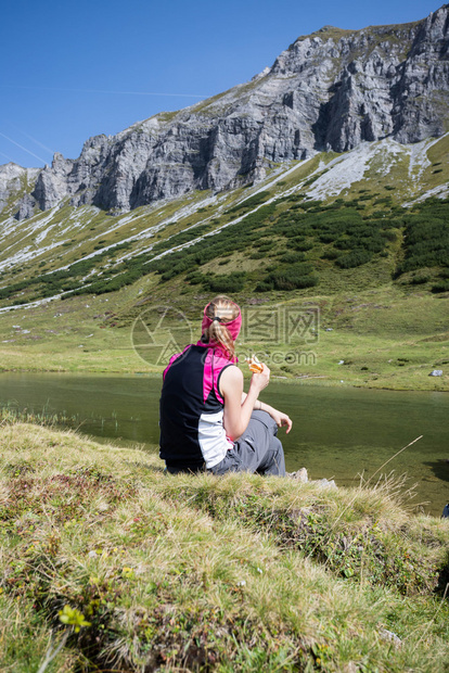 穿运动服的妇女正在徒步时休息坐在地上享受山和湖风景图片