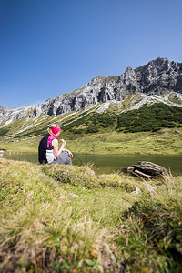 穿运动服的妇女正在徒步时休息坐在地上享受山和湖风景图片