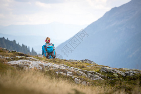 身穿运动服和背包的妇女坐在石土地上山享受风景图片