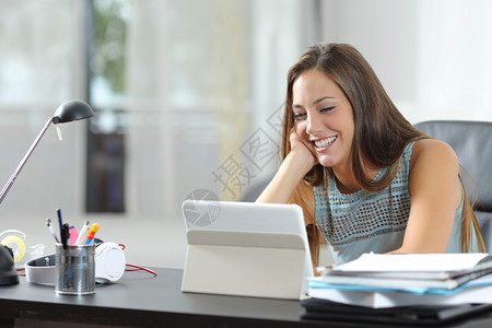 在家书桌上观看平板电脑媒体内容的快乐妇女图片