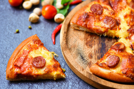 木制餐盘上的披萨片和深黑美味的红番茄辣椒叶子意大利传统披萨奶酪和Mozzarella猪肉香肠菠萝火腿酱图片