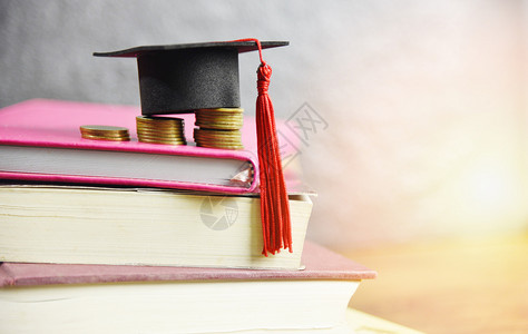 奖学金教育概念对在书桌和木上为赠款教育节省的硬币存款实行毕业上限背景图片