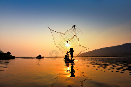 在湄公河中使用木造船抛出净日落或的亚洲渔网具有山地背景生命的Silhouette渔船图片