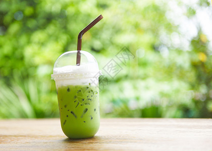 塑料杯中的冰绿茶符合自然背景的木制桌上绿色茶叶拿铁花和草图片