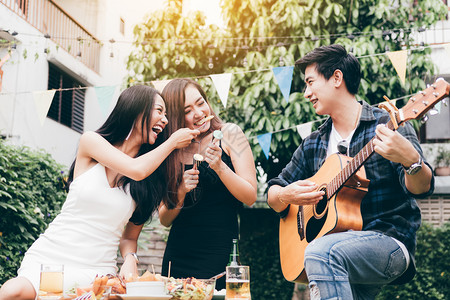 亚裔年轻女在户外家庭花园唱歌时与弹吉他的家伙一起喂饱朋友图片