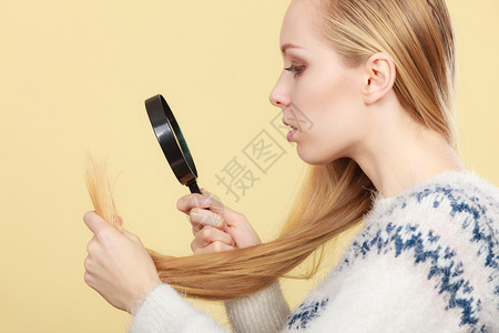 头发健康问题的概念不开心金发女人透过放大镜看金发的尽头图片