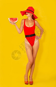 年轻女孩穿着明亮的红色泳衣和宽的红帽子在黄色背景上吃西瓜背景图片