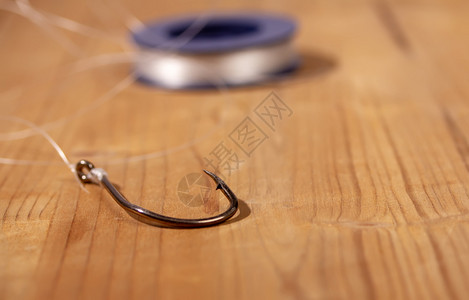 经典的大型钓鱼钩挂着一条细长的钓鱼线绑在木制背景的卷绳上图片