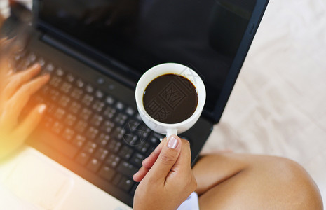上午早晨咖啡杯顶部风景手持咖啡杯和床上手提笔记本电脑的妇女手持咖啡杯的妇女图片