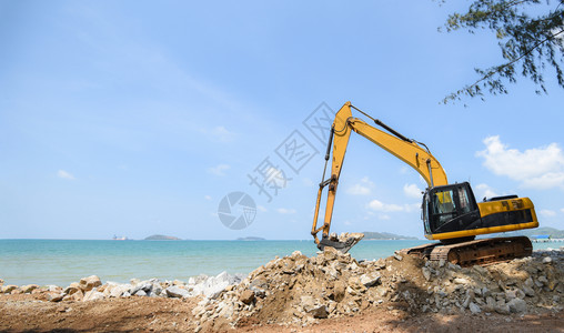 在海滨洋和蓝天空背景的建筑工地背鞋装载器上工作的挖土机掘石背景图片