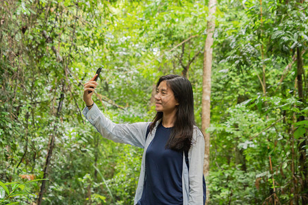 喜悦的亚洲女在泰国坎沙纳布里家公园旅行和户外度假时在热带森林的社交媒体上自拍图片
