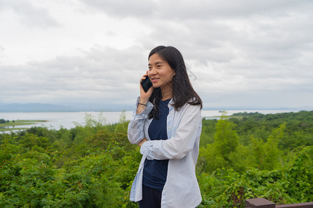 在泰公园旅行和户外度假期间快乐的亚洲妇女使用移动智能手机在热带森林社交媒体上聊天或致电朋友图片