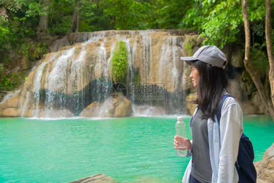 亚洲快乐妇女从热带森林瀑布的瓶子饮用水中在泰公园旅行和度假期间有树木图片