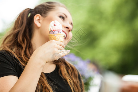 快乐的年轻女孩长棕色头发吃冰淇淋快乐地享受她的甜点在美丽夏日天气中与绿色公园对抗图片