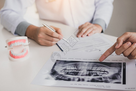 牙科医生手持笔与病人交谈用X光指着X照片说明药物和外科治疗的情况图片