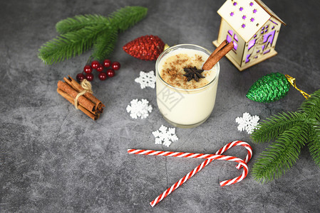 与传统圣诞节和冬季假日的肉桂松锥和豆饼果一起举行晚宴在眼镜和装饰的糖果罐中自制蛋酒图片