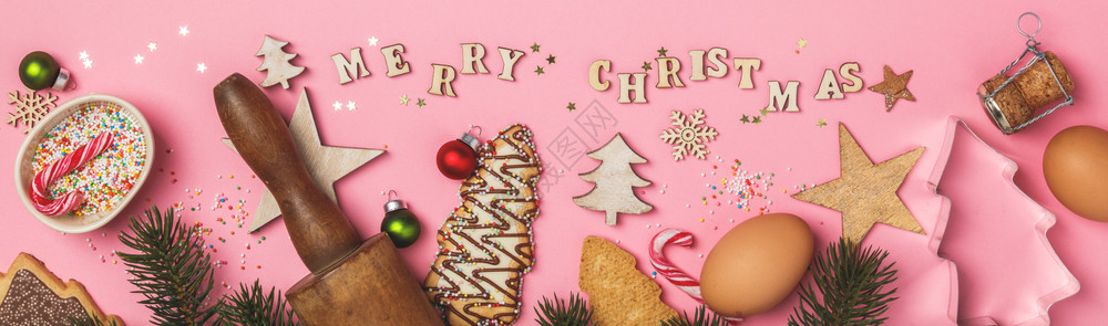 圣诞姜饼干以圣诞树的形状烘烤成份和圣诞快乐以粉红背景的木纸字母写成图片